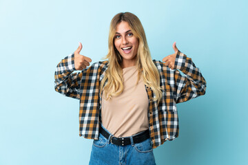 Obraz premium Young blonde Uruguayan isolated on blue background giving a thumbs up gesture