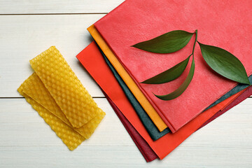 Colorful beeswax food wraps and fresh leaves on white wooden table, flat lay