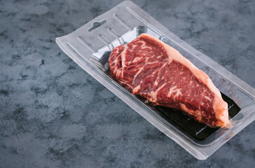 Vacuum packed Raw New York striploin beef steak on blue background with copy space.
