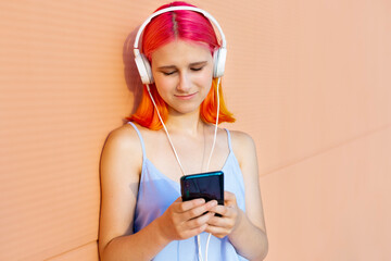 Teenage girl in headphones with dyed hair listens to music on a mobile phone.