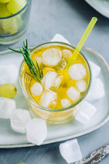 Refreshing summer drink in glass with ice cubes, green grape and rosemary on the table.