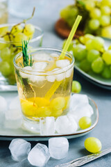 Refreshing summer drink in glass with ice cubes, green grape and rosemary on the table.