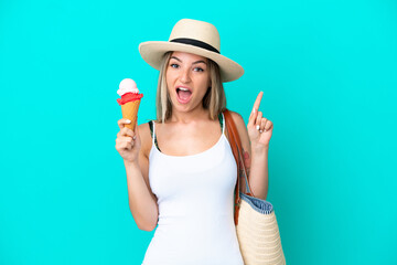 Young Romanian woman holding ice cream and beach bag isolated on blue background pointing up a great idea