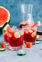 Watermelon cocktail in a glass with cucumber slice and ice cubes on the table. Refreshing drink