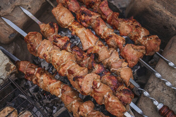 Pieces of meat fried on metal skewers. Cooking shish kebab from raw meat on coals by the fire, in the open air. Pieces of meat and mushrooms are fried in a frying pan.