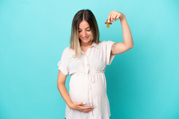 Young Romanian woman isolated on blue background pregnant and holding a pacifier