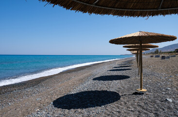 Tropical beach umbrellas providing sunshade for swimmers at an empty beach. Summer vacations.