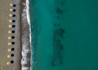 Fototapeta na wymiar Aerial view from a flying drone of beach umbrellas in a row on an empty beach with braking waves.