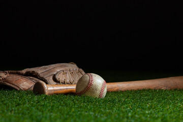 Old baseball bat and mitt low angle on grass field and dark background - Powered by Adobe