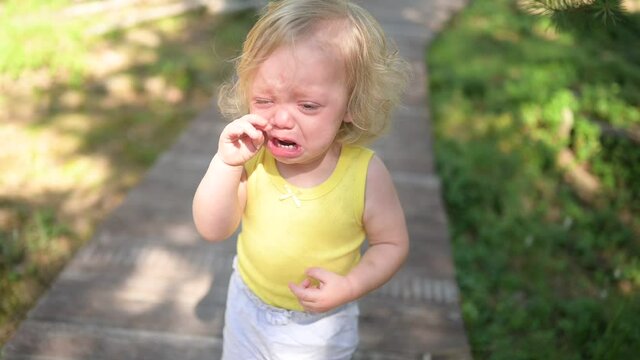 Close up portrait of little funny cute blonde girl child toddler in yellow bodysuit crying outside at summer. Childish tantrum. Healthy childhood concept