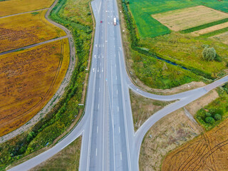 Panoramic view over a field with green grass and golden wheat. The cars are moving on the road.