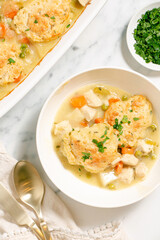 Homemade chicken and dumplings with carrots, peas and potatoes in a white baking dish