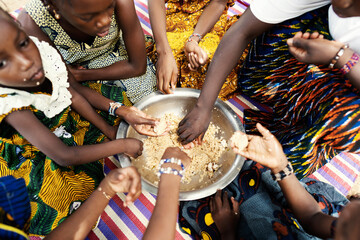 Group of black African girls sitting on a mat, dividing their frugal meal, eating with their hands...