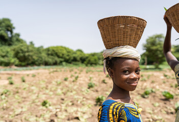 Smiling little African girl with an empty basket on her head returning home from the village market...
