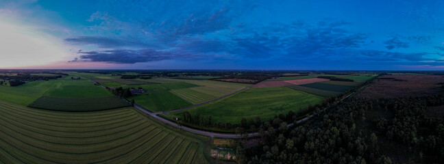 Blue hour aerial 180 degrees panorama of Dutch farmland landscape with colorful sunset in the sky. Agriculture farmland food industry.