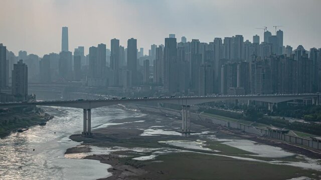 Chongqing cityscape with low water level river. Suffering drought conditions major Chinese city timelapse. Dried up riverbed at sunset in populous city.
