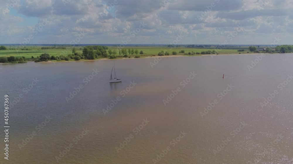 Wall mural An aerial shot of a sailboat in the middle of a lake next to a beautiful green landscape fie in 4K