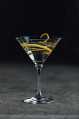 martini glass with long lemon twist against black 