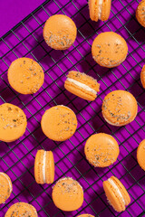 Orange macarons cooling on a wire rack with a purple background
