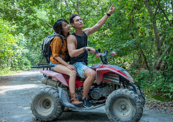 Handsome man pointing the finger at his girlfriend to look at the beautiful scenery while riding an ATV in  forest