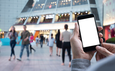 Mockup of man hand holding blank screen mobile phone with crowd people walking at shopping centre...