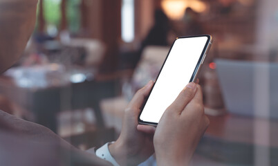 Cell phone mockup image blank white screen.  Woman hand holding, using mobile phone in coffee shop, close up