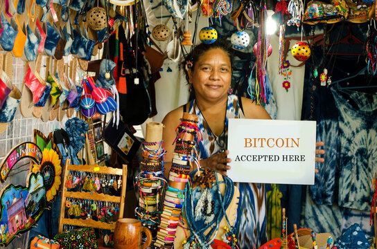 Woman hand craft seller showing a sign that says that bitcoin is accepted in her shop
