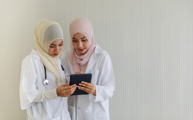 Two young female Muslim doctors are working and discussing using laptop and tablet at the hospital office room