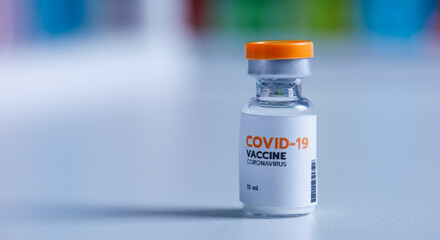 Close up shot of 10 ml coronavirus covid 19 vaccine in small glass vial bottle with red label for protection prevention epidemic pandemic virus outbreak around world in laboratory blurred background