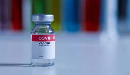 Close up shot of 10 ml coronavirus covid 19 vaccine in small glass vial bottle with red label for protection prevention epidemic pandemic virus outbreak around world in laboratory blurred background