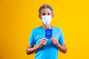 elderly man holding brazilian work card in hands and with surgical mask on his face. Concept of...