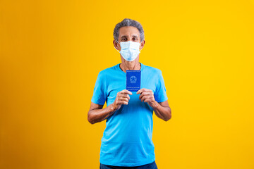 elderly man holding brazilian work card in hands and with surgical mask on his face. Concept of...