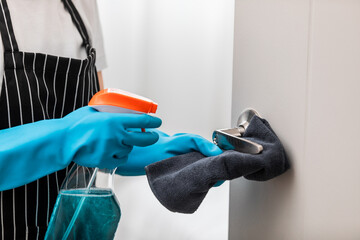Close up, Housekeeper wearing protective gloves cleaning door handle using alcohol and liquid cleaning solution to prevent coronavirus (COVID-19) infection, Disinfection and Hygiene home concept.