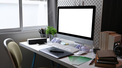 Graphic designer workplace with computer, graphic tablet and books on white desk.
