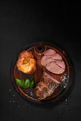 Roastbeef, yorkshire puddnings, basil leaves on a wooden cutting bords. Rustic style. Top wiev vertical photo .