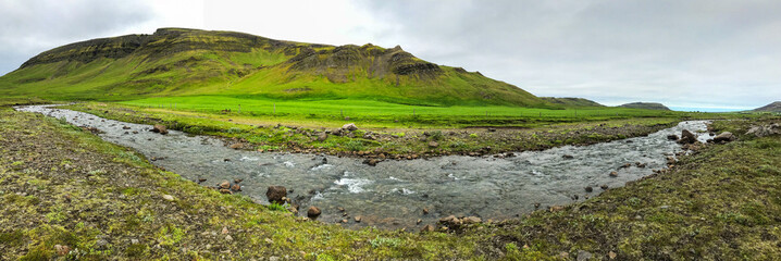 Summer Iceland panorama on winding river among fields and hills of green grass.