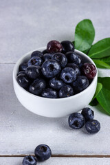 Freshly picked blueberries in a bowl. Juicy and fresh blueberries with green leaves on rustic table. Concept for healthy eating and nutrition
