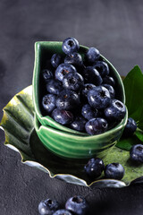 Freshly picked blueberries in a bowl. Juicy and fresh blueberries with green leaves on rustic table. Concept for healthy eating and nutrition