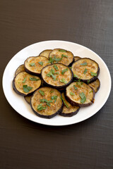 Homemade Organic Roasted Eggplant on a white plate on a black surface, side view.