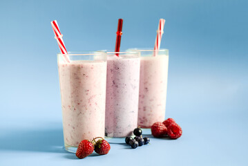 Milkshakes with the addition of raspberries, strawberries and blueberries on a light background close-up. Cocktails made of ice cream, milk and berries on a blue background