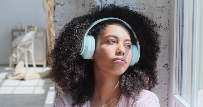 A gorgeous mixed-race woman is captivated by the pleasant sensations as she listens to relaxing music on her phone. A break from freelance work, as well as a search for inspiration and creativity