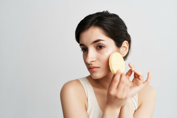 brunette applies a sponge cream on her face clean skin