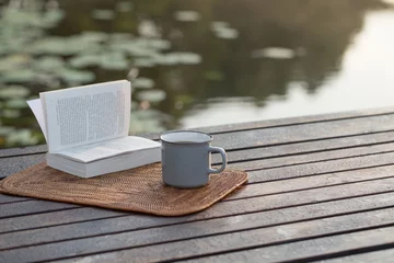 Fototapeten cup of coffee and book on wooden pier on summer lake © Maya Kruchancova