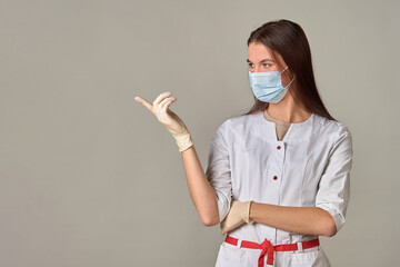 A female doctor in a medical mask points to an empty place, copy space