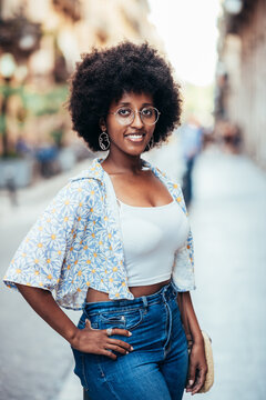 young african woman standing on the streets of Barcelona and looking at camera. she is posing with one hand on her hip and smiling