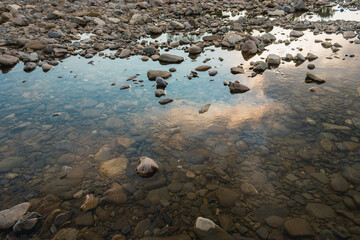 The sun is reflected at sunset in the water of a mountain river. Crystal clear water in the river with stones along the shore.