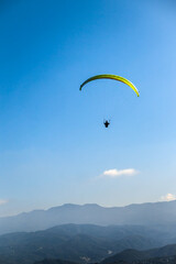 A yellow paraglider is flying over the mountain