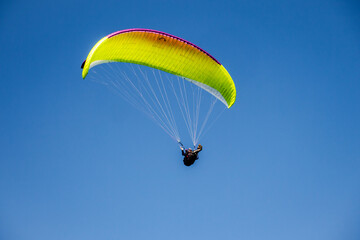 A yellow paraglider is flying in the sky