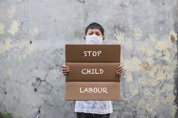 Asian boy in medical mask holding letter board says Stop Child Labour campaign with hand print in...