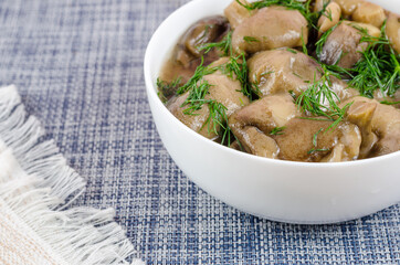 Marinated mushrooms in a white ceramic bowl with dill. The white